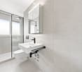 Modern bathroom with a white sink, toilet, mirror, and glass-enclosed shower. Light-colored tiles and sleek fixtures.
