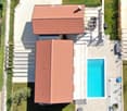 Aerial view of a two-story house with a red-tiled roof, surrounded by a well-maintained garden and a swimming pool.