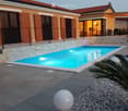 Modern outdoor area with a swimming pool, surrounded by a stone border, a palm tree, and a decorative spherical light fixture on a gravel bed.