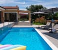 A modern outdoor area featuring a swimming pool, lounge chairs, an umbrella, and a patio area with steps leading to a house entrance.