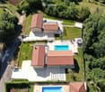 Aerial view of a modern two-story house with red-tiled roofs, surrounded by a well-maintained garden and featuring two swimming pools in the outdoor area.