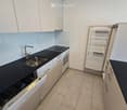 Modern kitchen with white cabinets, black countertops, stainless steel sink, faucet, oven, dishwasher, and open refrigerator.