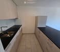 Empty kitchen with white cabinets, black countertops, and a stainless steel sink.
