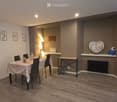 Dining area with a wooden table, chairs, vase, lamp, radiator, heart-shaped wall decoration, and picture frame.
