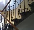 Staircase with wooden handrail and ornate metal balustrade, carpeted steps, light-colored walls, and a window providing natural light.