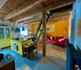 Open-plan living and dining area with exposed wooden beams, a red leather sofa, a glass coffee table, a yellow kitchen island, and pendant lights.