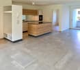Modern kitchen with light wooden cabinets, a central island, and a large open space. The floor is tiled in a light beige color, and there is a sliding glass door leading to another room.