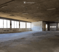 Empty industrial-style room with concrete floors and walls, large windows, and exposed ceiling beams. No furniture or equipment present.