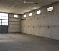 Empty industrial-style room with concrete walls and floor, large windows, and a metal door.