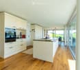 Modern kitchen with white cabinets, wooden flooring, island, and large windows offering a view.