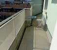 Balcony with tiled floor, metal railing, small round table, and folding chair, overlooking cityscape with rooftops and mountains.