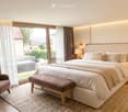 Modern bedroom with a large bed, nightstands, a bench at the foot of the bed, a chair, and a wicker basket on the floor.