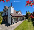 Two-story house with red-tiled roof, white and red facade, chimney, and well-maintained garden with lawn, patio, and outdoor seating area.