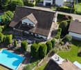 Aerial view of a two-story house with a well-maintained garden, a swimming pool, and surrounding greenery.