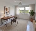 Modern, well-lit room with a wooden desk, chair, table lamp, picture frame, potted plant, and decorative vases.