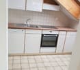 Modern kitchen with white cabinets, a sink, dishwasher, and oven, featuring tiled walls and a wooden countertop.