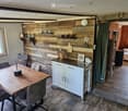 A cozy, rustic kitchen and living area with wooden walls, a dining table with chairs, a white kitchen cabinet, and a small living space with a sofa.