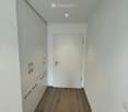 Empty hallway with white walls, wooden flooring, and a white door at the end.