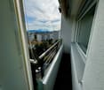 Balcony with metal railing, overlooking a cityscape with buildings, trees, and parked cars.