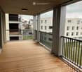 Balcony with wooden decking, metal railing, and view of surrounding buildings and greenery.