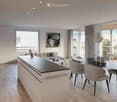 Modern, open-plan living and dining area with a white kitchen island, grey sofa, dining table with chairs, and large windows leading to a balcony.