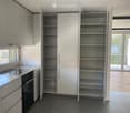 Modern kitchen with white cabinets, a sink, and an oven. The cabinets are open, revealing empty shelves.
