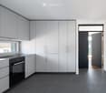 Modern kitchen with white cabinets, black oven, and dark tiled floor. Features a large window and an open doorway leading to another room.