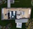 Top-down floor plan of a modern, compact house with a living area, bedroom, bathroom, and outdoor patio. Features include a staircase leading to a loft area, a small kitchen, and a covered outdoor seating area with a table and chairs.