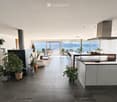 Open-plan living and kitchen area with large windows offering a scenic view, featuring a sofa, coffee table, kitchen island, bookshelf, and potted plants.