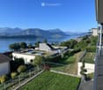Garden area with a view of a lake and mountains, featuring a small lawn, potted plants, and a modern building with a balcony.