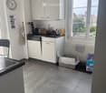 Modern kitchen with white cabinets, black countertop, sink, dishwasher, and various appliances. Features a tiled floor, a window with a view, and a cat litter box in the corner.