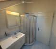 Modern bathroom with a white sink, mirror with built-in lighting, a round glass shower enclosure, and a radiator. The walls are tiled with a decorative border near the ceiling.
