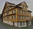 Two-story yellow house with multiple windows, red-tiled roof, and white trim around windows and roofline.