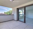 Balcony with tiled floor, large glass sliding doors, and a view of the surrounding area with trees and rooftops.