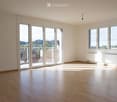 Empty room with wooden flooring, large windows, and sliding glass doors leading to a balcony.