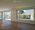 Empty room with wooden flooring, large windows, and sliding doors leading to an outdoor area.
