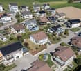 Aerial view of a residential neighborhood with multiple houses, solar panels on roofs, driveways, and surrounding greenery.