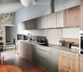 Modern kitchen with wooden cabinets, stainless steel countertops, induction stove, sink, oven, toaster, trash bin, chandelier