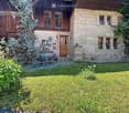 Two-story house with stone and wooden exterior, multiple windows, and a small garden area.
