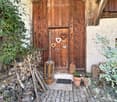 Entrance to a rustic building with a wooden door adorned with heart-shaped decorations, a lantern, potted plants, and a cobblestone pathway.