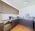 Modern kitchen with grey cabinets, stainless steel appliances, wooden flooring, and various kitchen items on the counter.