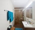 Modern bathroom with white tiles, a glass-enclosed shower, a large mirror, a sink with a cabinet, and a towel hanging on a rack.