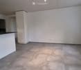 Empty kitchen with white cabinets, a black countertop, and a large window letting in natural light. The floor is tiled, and the space is clean and uncluttered.