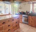 Bright kitchen with wooden island, induction cooktop, oven, sink, and cabinets. Features a vase with flowers and a hanging light fixture.