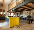Open-plan kitchen and dining area with a yellow kitchen island, stainless steel appliances, dining table with chairs, and various kitchen items on counters.
