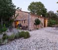 A rustic stone house with a gravel courtyard, outdoor seating, and greenery.
