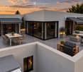 Modern rooftop terrace with a dining area, lounge seating, barbecue, and potted plants, overlooking a scenic sunset view.