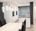 Modern kitchen and dining area with white cabinets, a central island, pendant lights, and a dining table with black leather chairs.