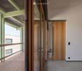 Modern hallway with wooden doors, glass partitions, and a view onto a wooden decked balcony area.