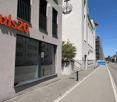 Modern building facade with large windows and a sign reading "puls20" in orange letters. The building has a clean, contemporary design with a small staircase leading up to the entrance.